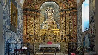 Interior de igreja ornamentado, com altar central, decorações detalhadas nas paredes e uma grande janela.