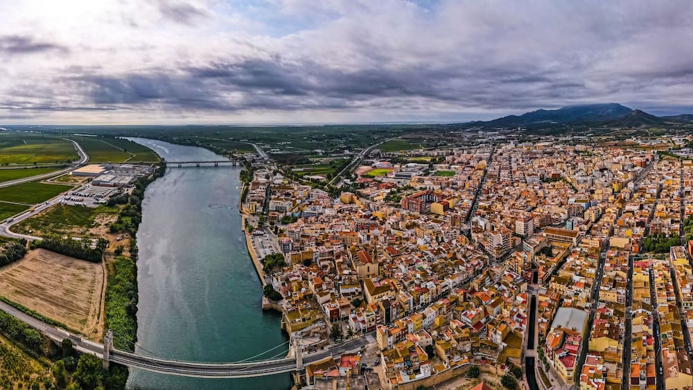 An aerial view of a city with a river, green fields, and a bridge.