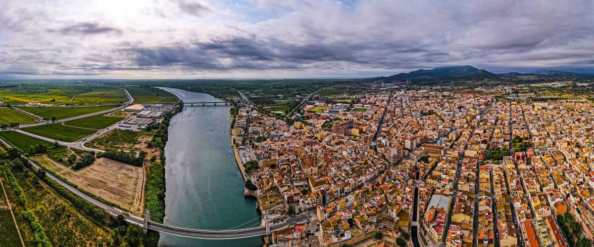An aerial view of a city with a river, green fields, and a bridge.