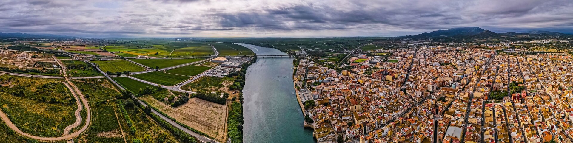 An aerial view of a city with a river, green fields, and a bridge.