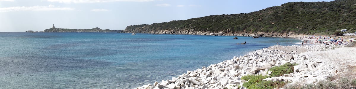 Une plage de rochers bordée d’une eau d’un bleu limpide, une île lointaine et un paysage vallonné.