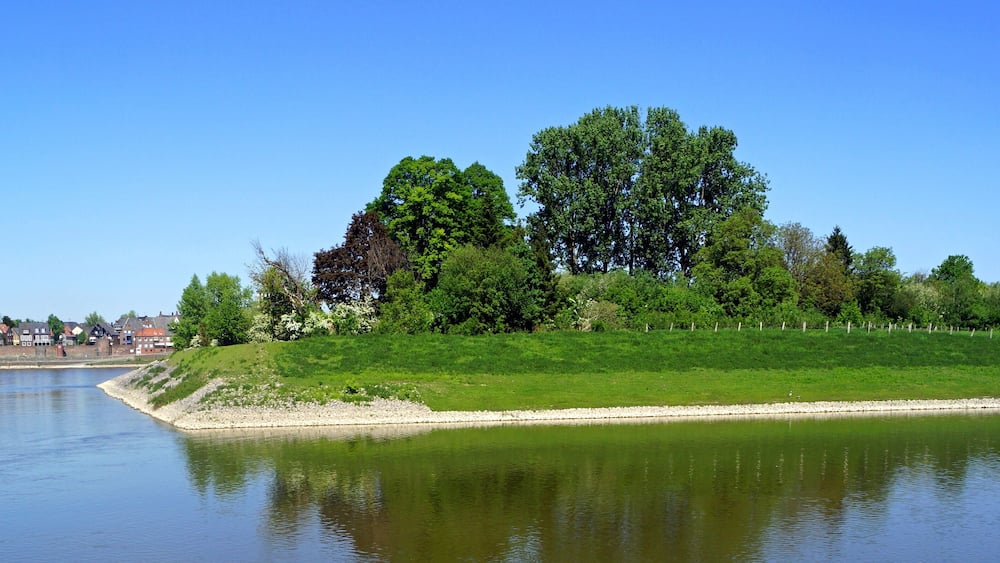 A calm river with a grassy embankment and trees.