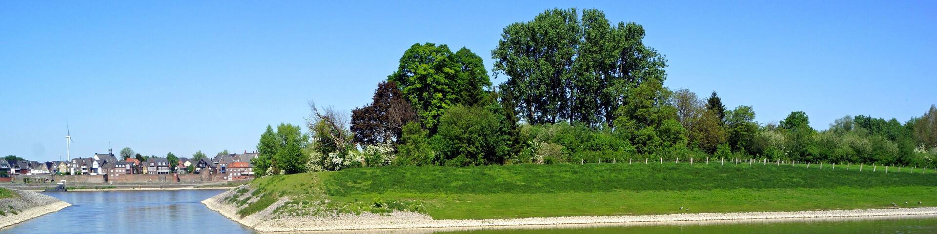 A calm river with a grassy embankment and trees.