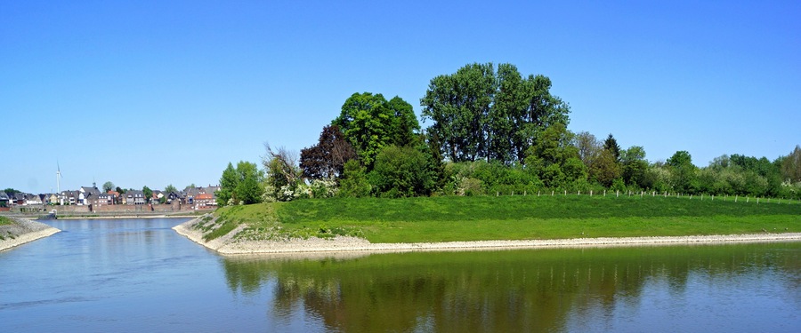 Ein ruhiger Fluss mit einer grünen Uferböschung und Bäumen.