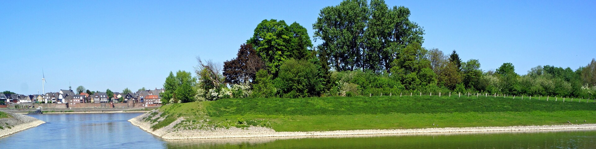 A calm river with a grassy embankment and trees.