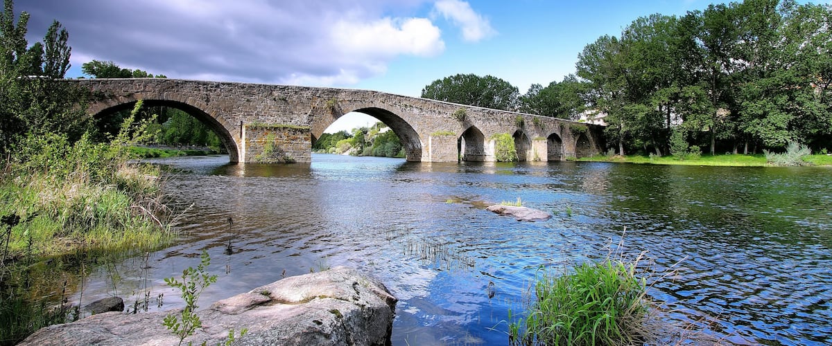 A stone bridge over a calm river surrounded by greenery.