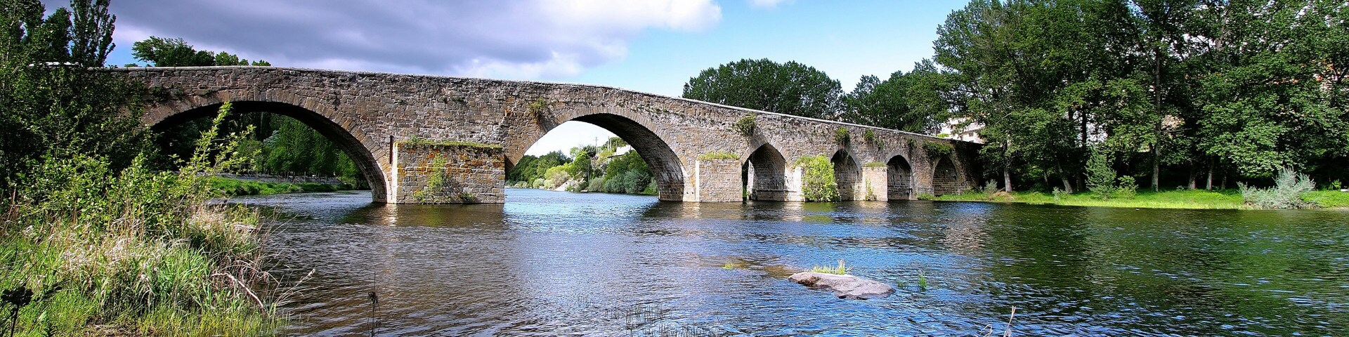 A stone bridge over a calm river surrounded by greenery.