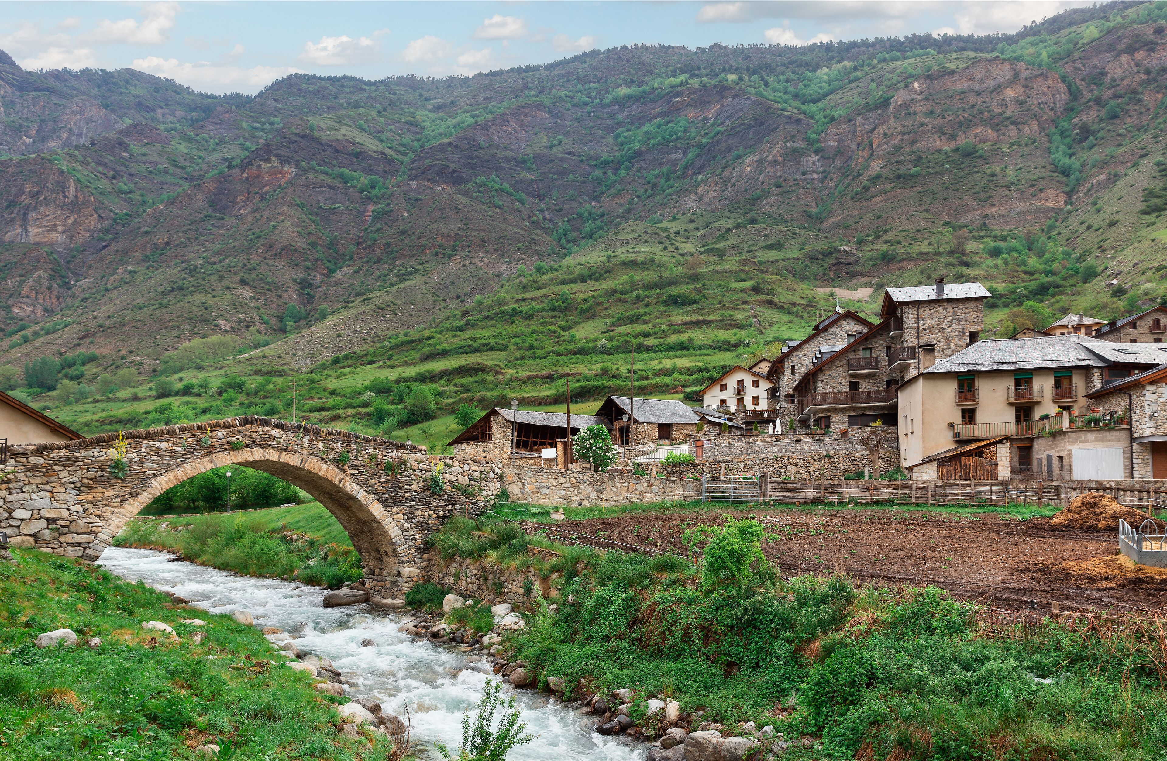 A stone bridge over a river, surrounded by lush green hills and traditional stone buildings.