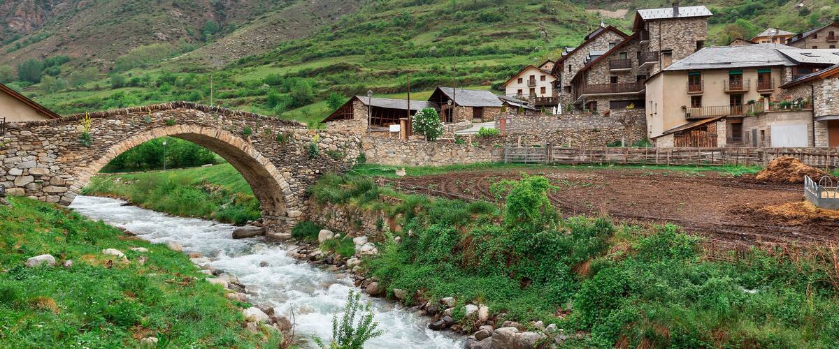 A stone bridge over a river, surrounded by lush green hills and traditional stone buildings.