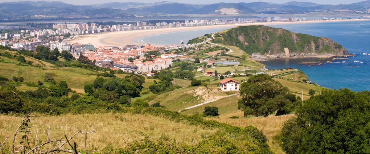 A coastal cityscape with a beach, hills, and a castle.