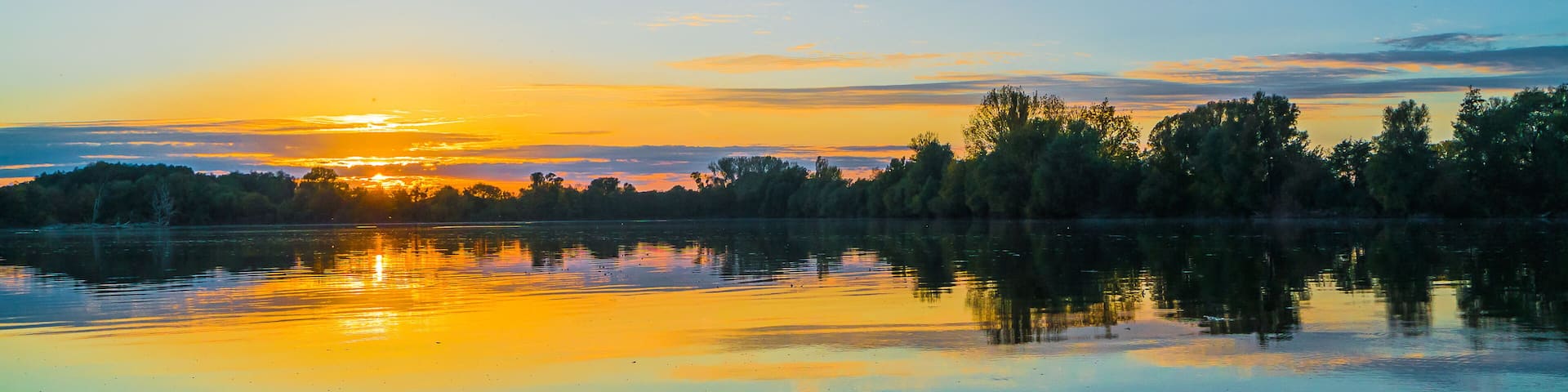 A calm lake at sunset with trees reflecting the sky.