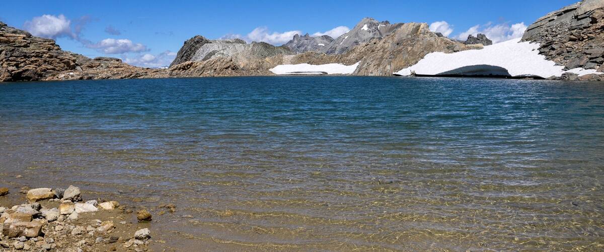 A clear lake surrounded by rocky mountains with patches of snow.