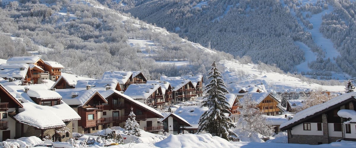A snow-covered mountain village with wooden houses and a ski slope.