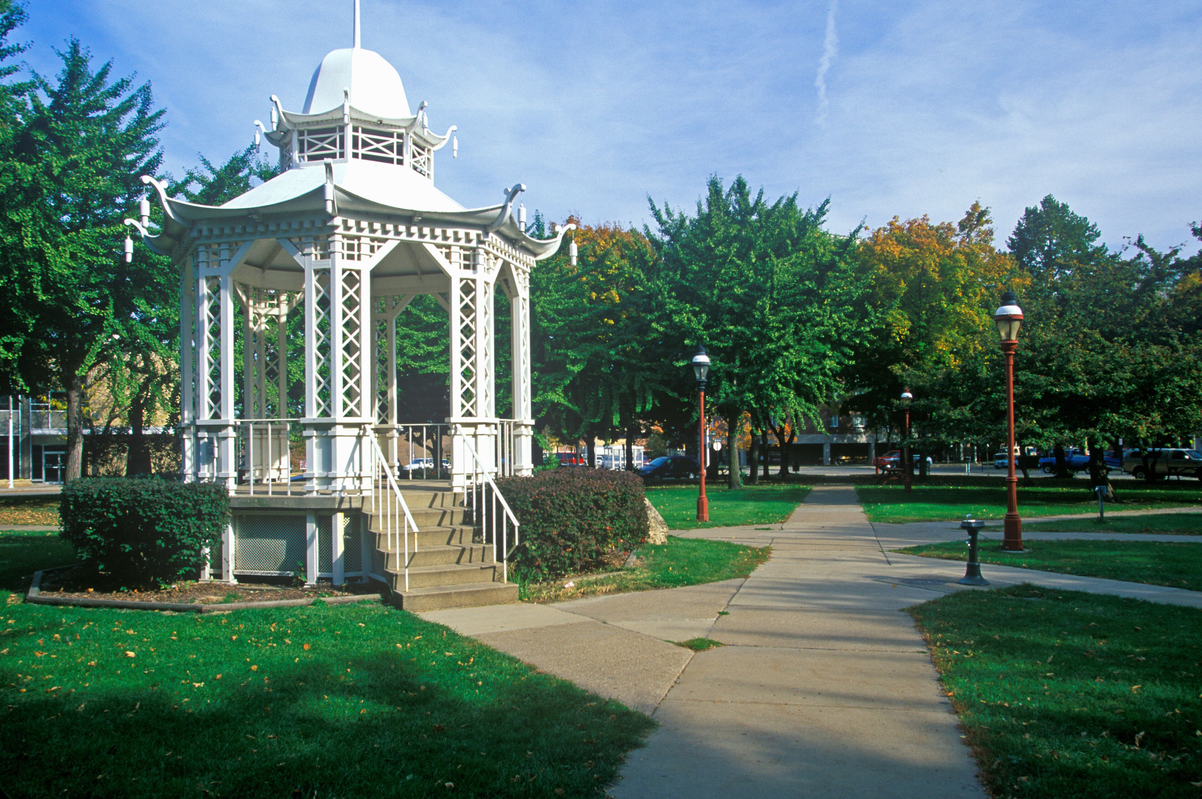 A white gazebo with a dome roof and intricate lattice design, surrounded by lush green grass and trees.