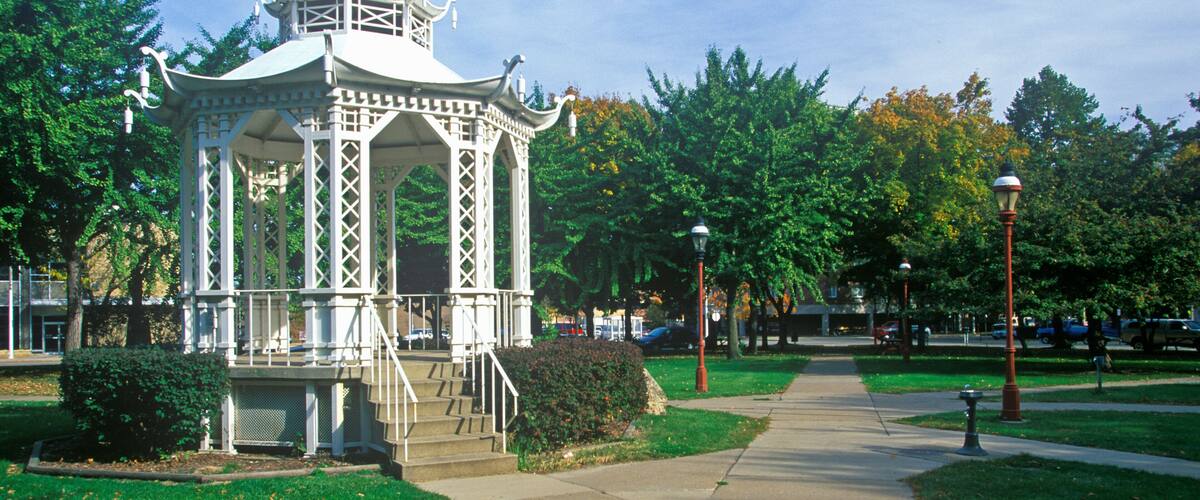 A white gazebo with a dome roof and intricate lattice design, surrounded by lush green grass and trees.