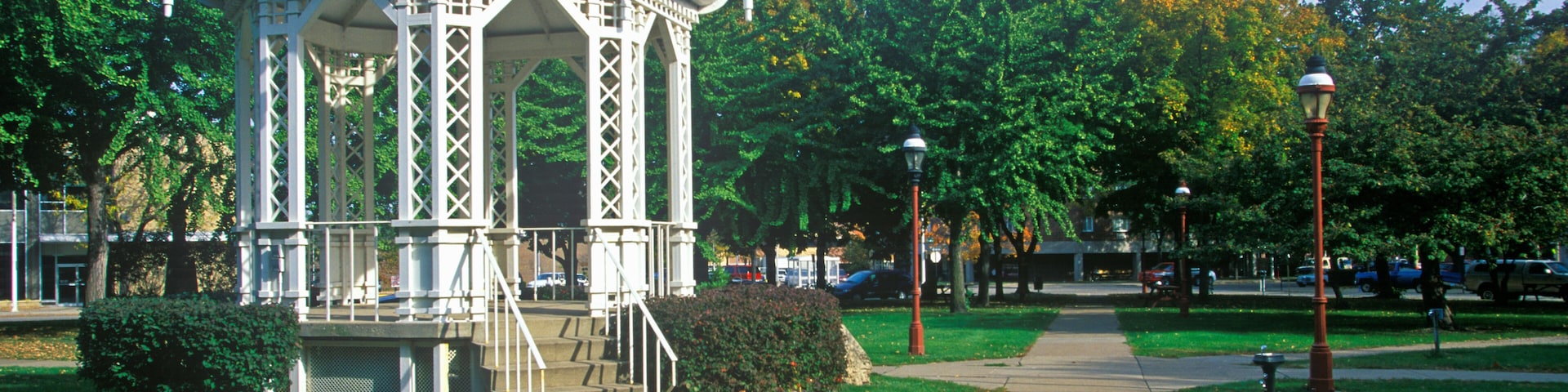 A white gazebo with a dome roof and intricate lattice design, surrounded by lush green grass and trees.