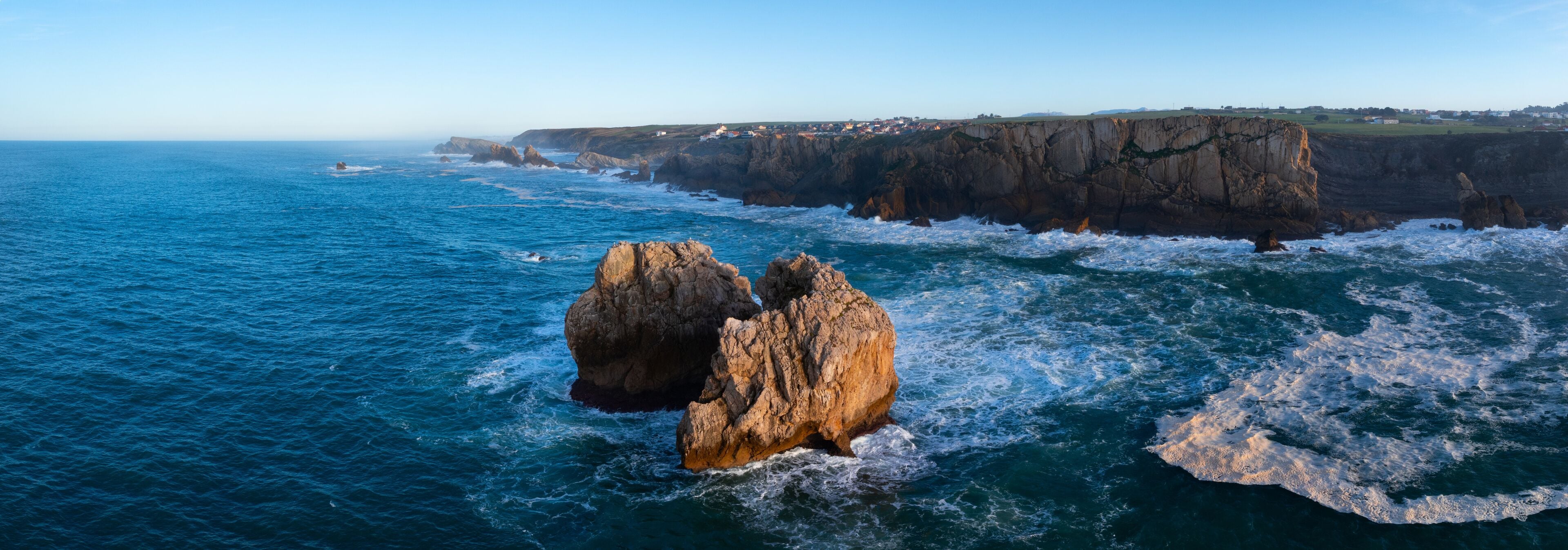 A coastal landscape with prominent rock formations and a clear view of the ocean.
