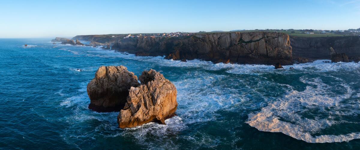 A coastal landscape with prominent rock formations and a clear view of the ocean.