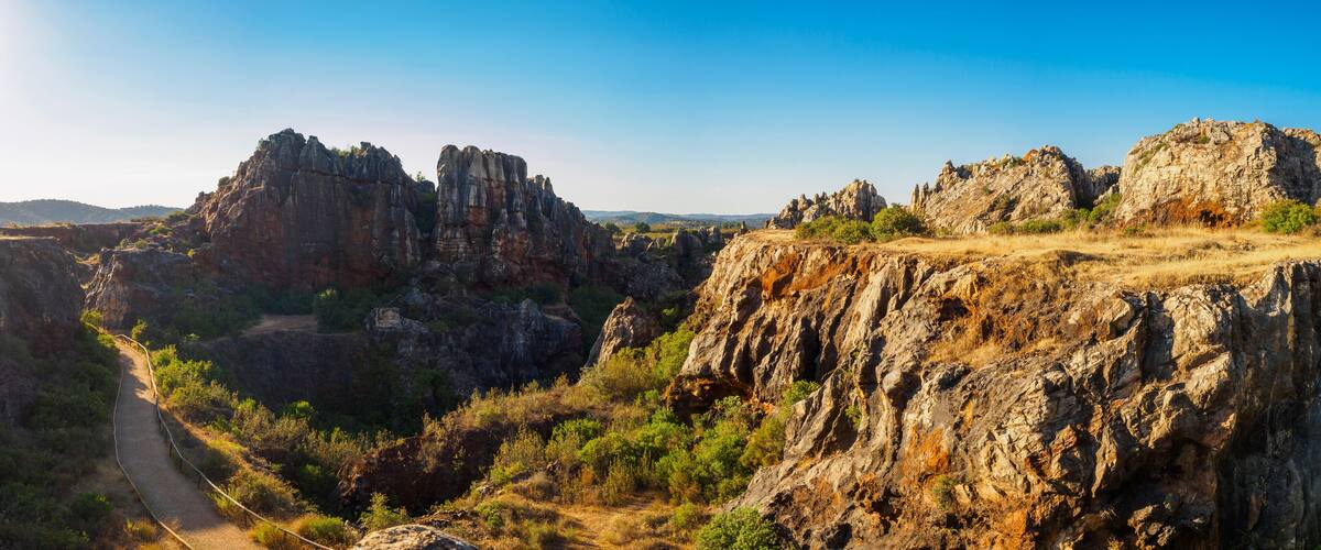 A rugged canyon landscape with a dirt path winding through rocky outcrops and sparse vegetation.