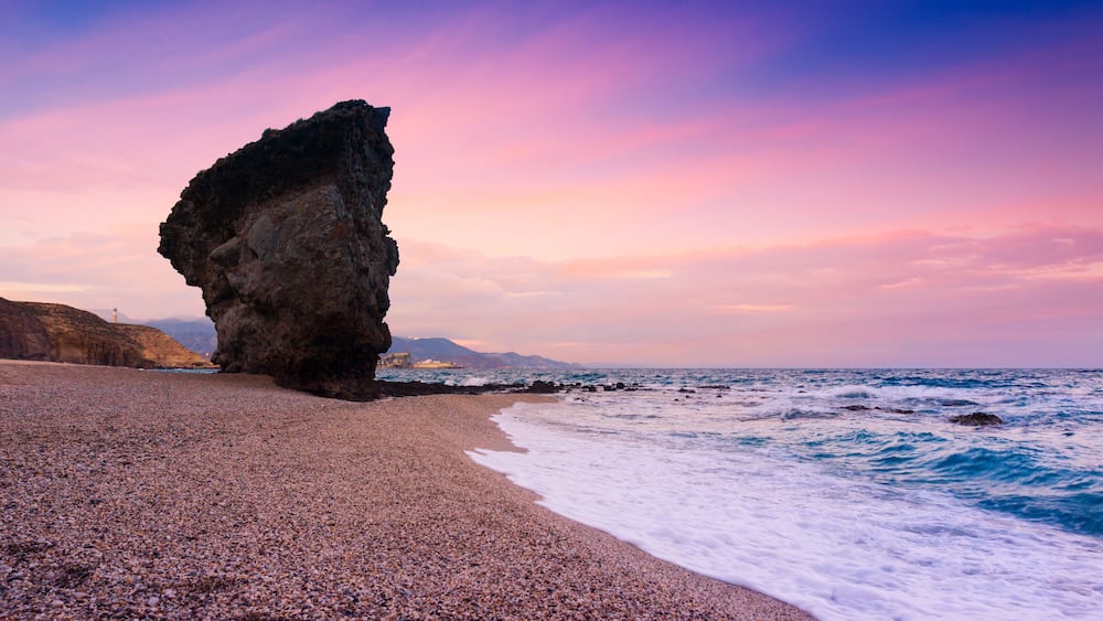 Une plage de galets avec une grande formation rocheuse et l’océan.