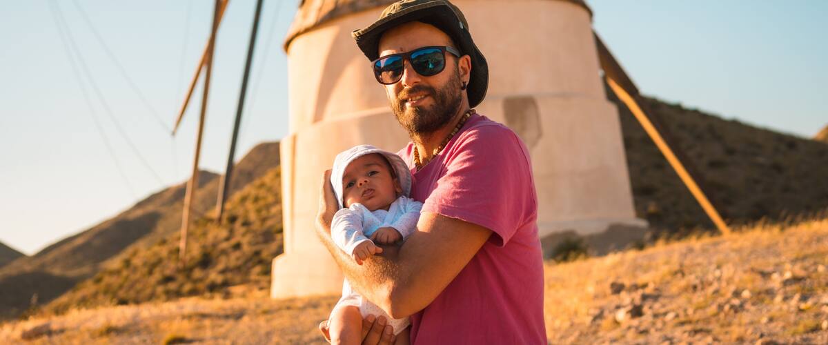 A man holding a baby in front of a windmill.