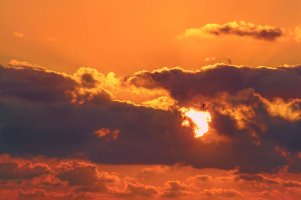 A sunset over the ocean with a sailboat.