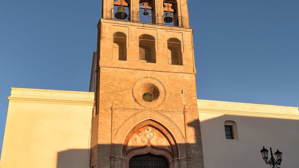 A tall brick tower with a clock and bells, set against a clear sky.