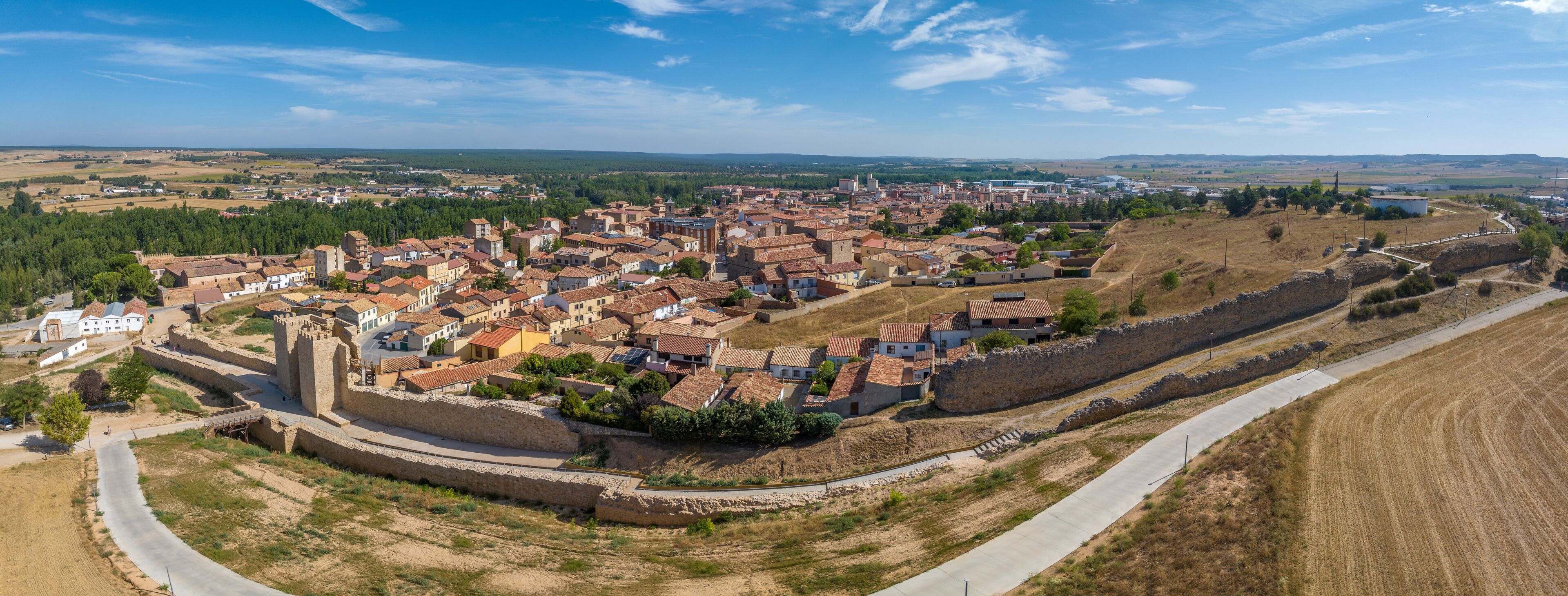 A historic town with a fortified wall, terraced houses, and a mix of open fields and forested areas.
