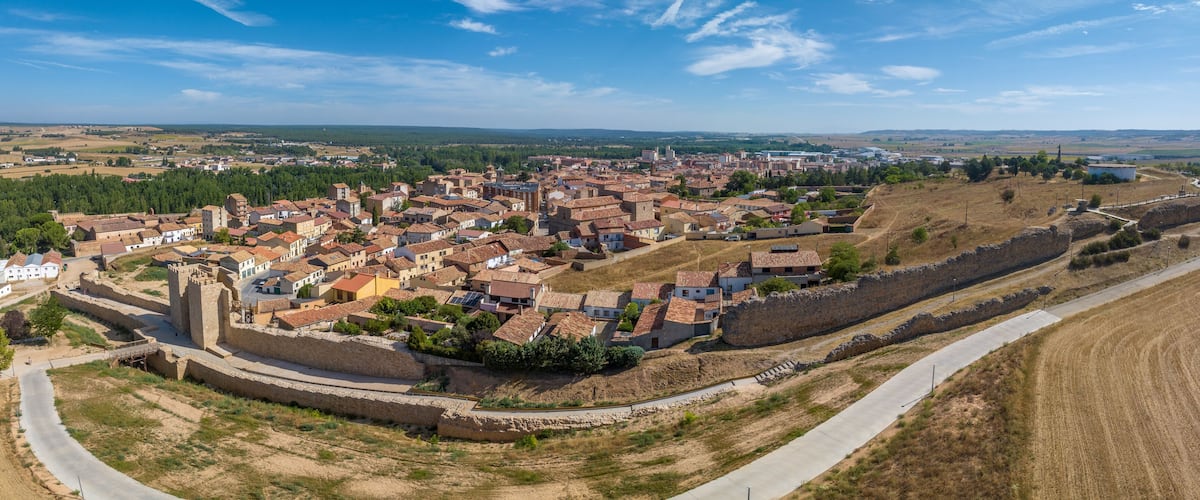 A historic town with a fortified wall, terraced houses, and a mix of open fields and forested areas.