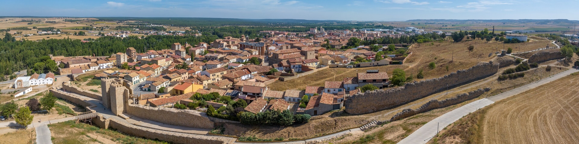 A historic town with a fortified wall, terraced houses, and a mix of open fields and forested areas.