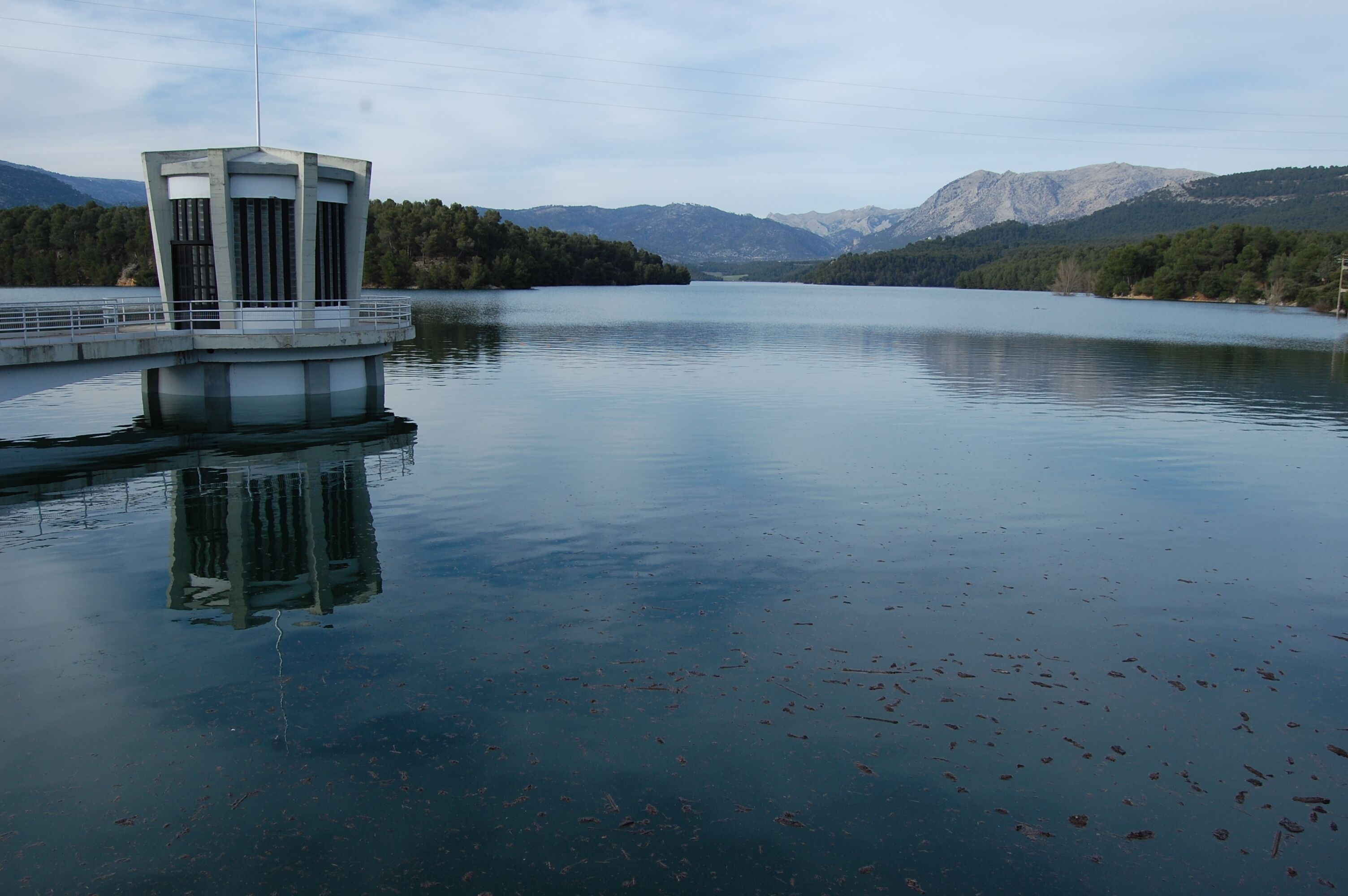 A calm lake with a small island structure, surrounded by mountains and dense forests.