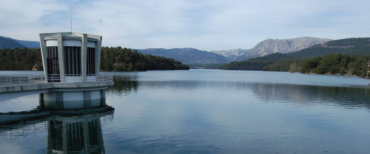 A calm lake with a small island structure, surrounded by mountains and dense forests.