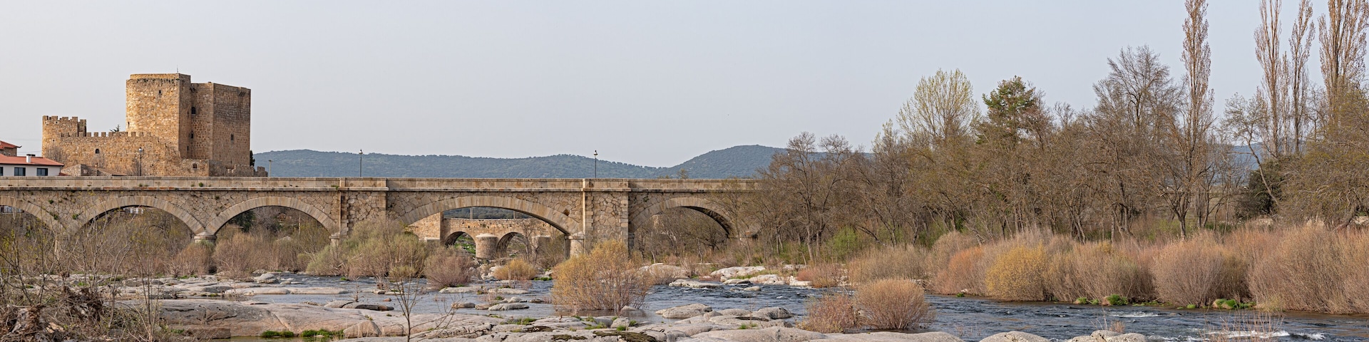 A stone bridge over a river with a castle in the background.