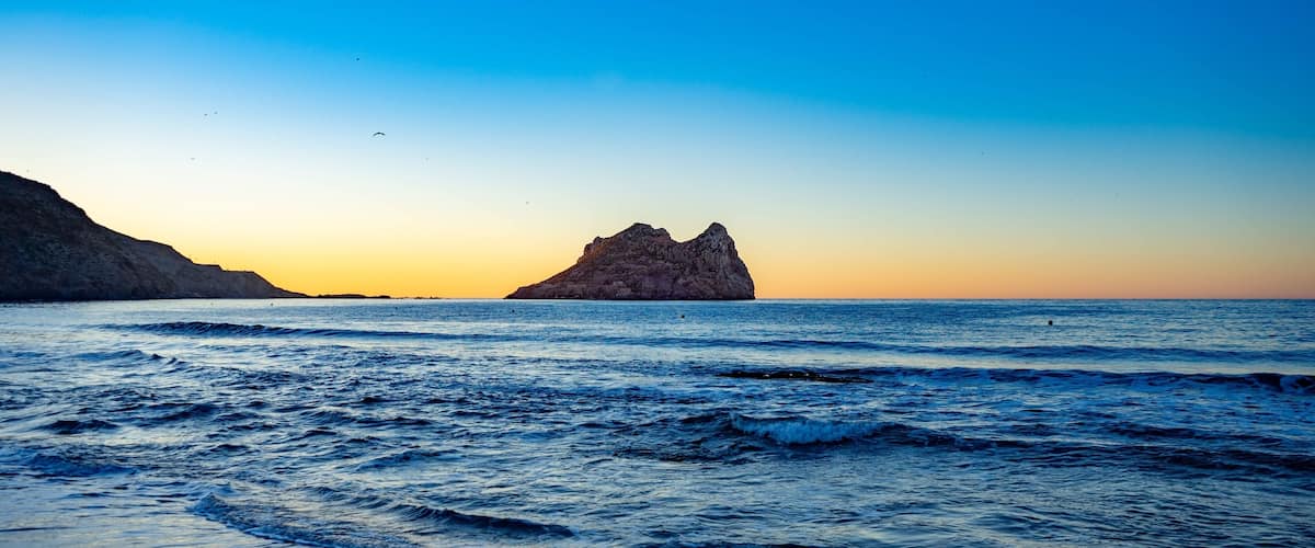 A rocky island in the ocean with waves crashing onto the shore.