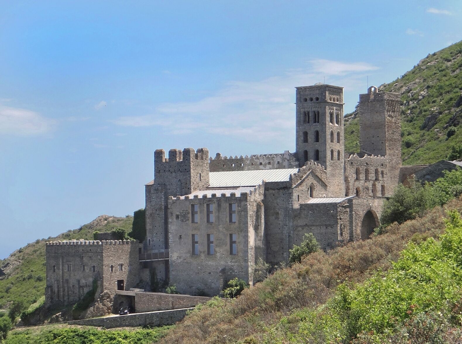 A medieval castle with a prominent tower, surrounded by lush greenery and hills.