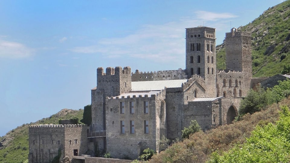 A medieval castle with a prominent tower, surrounded by lush greenery and hills.