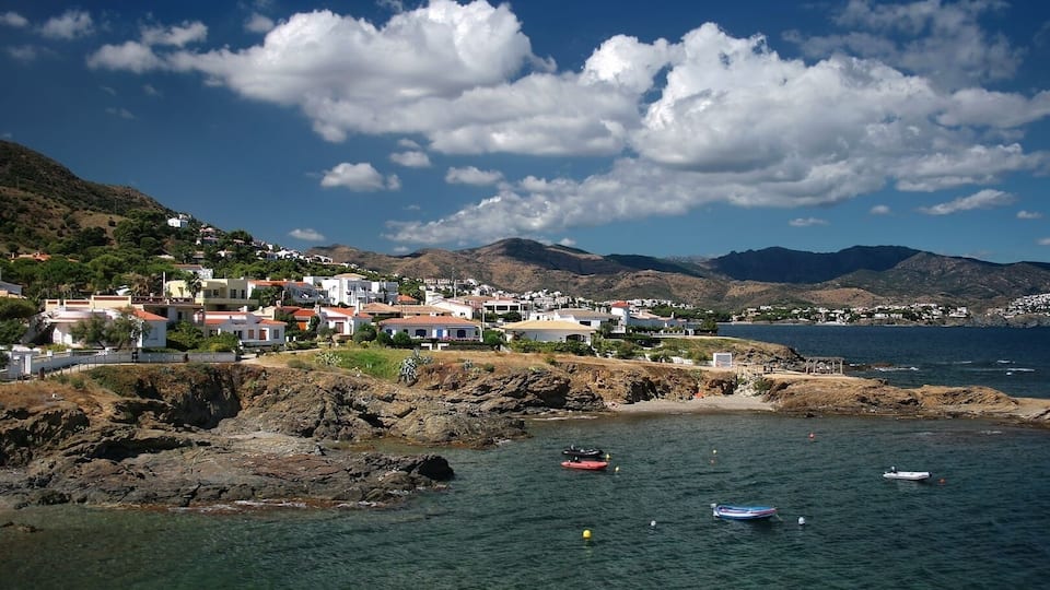 A coastal town with buildings on a hillside, clear blue water, and boats.