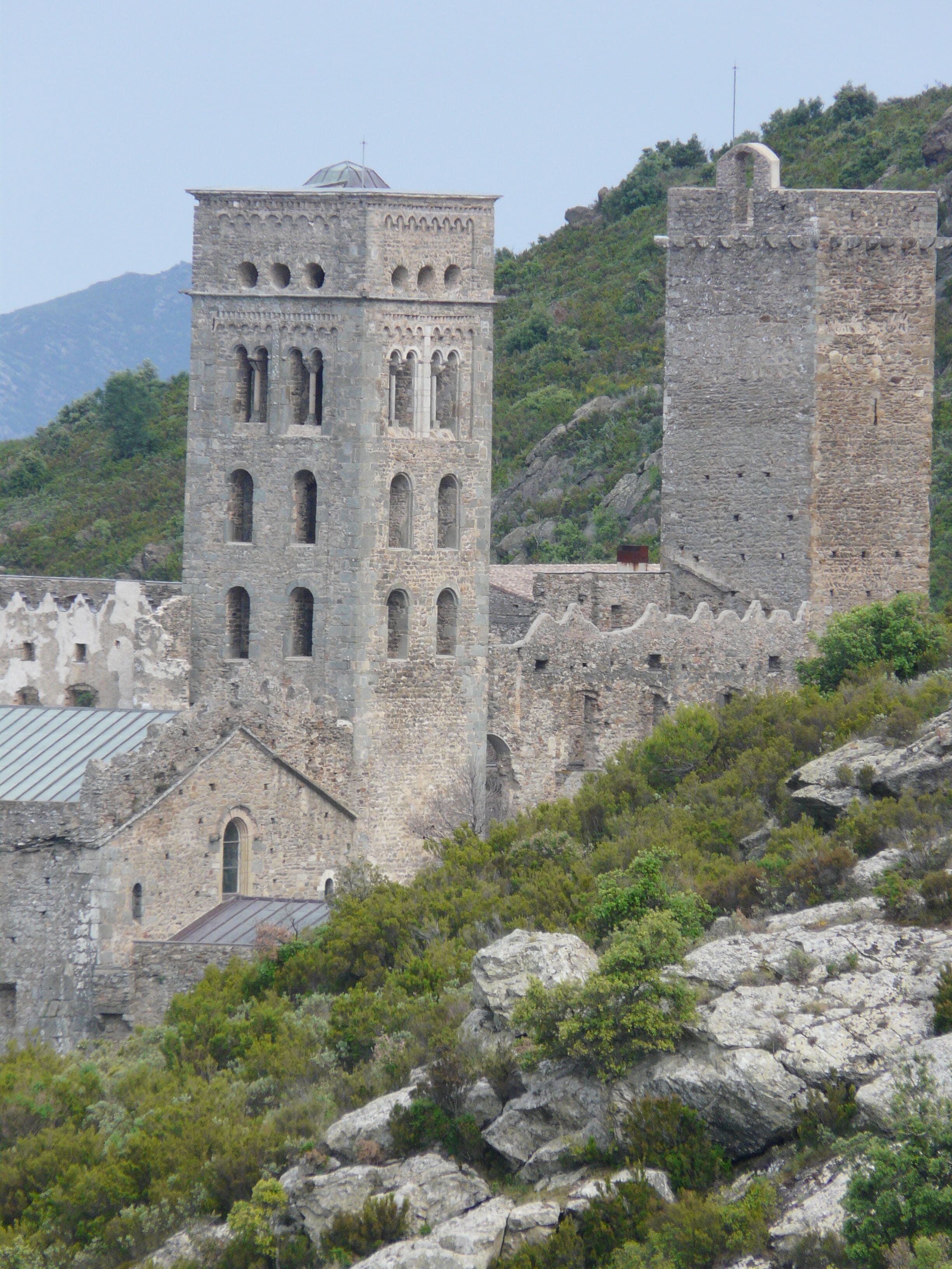 A historic stone tower with arched windows and a dome, surrounded by rocky terrain and greenery.