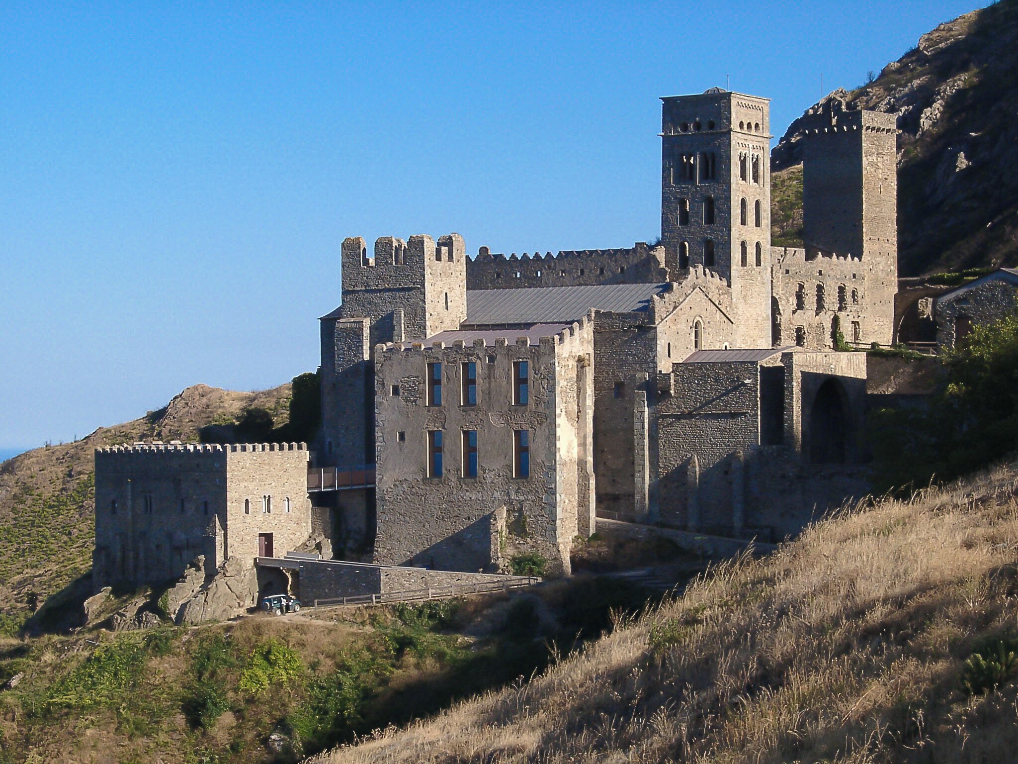 A medieval castle with multiple towers and a large entrance gate, situated on a hillside.
