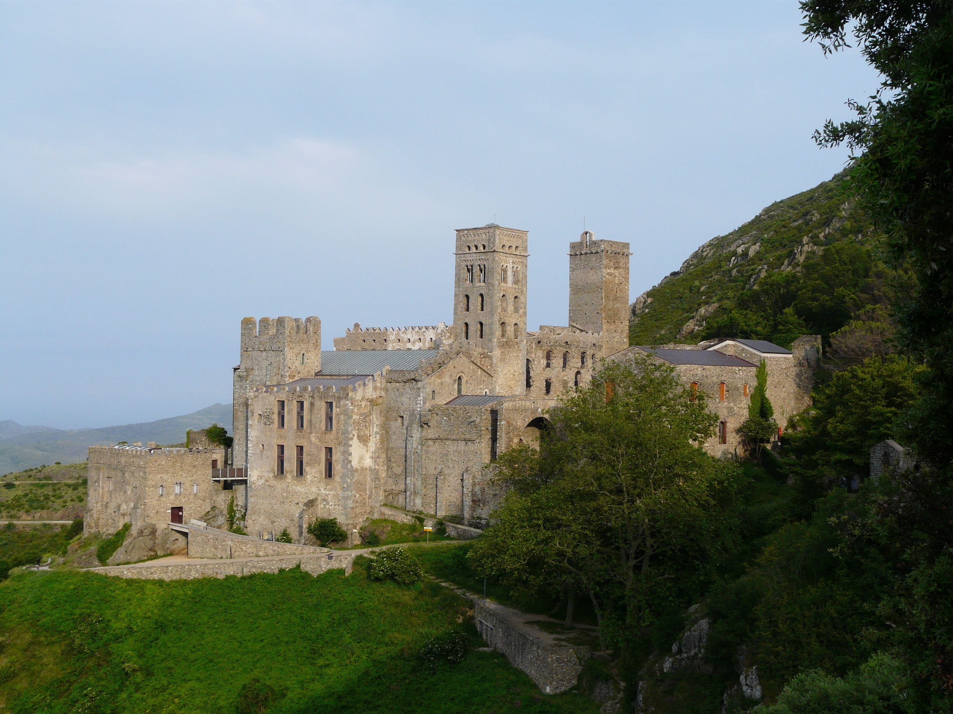 A historic stone castle with multiple towers and battlements, surrounded by lush greenery and hills.