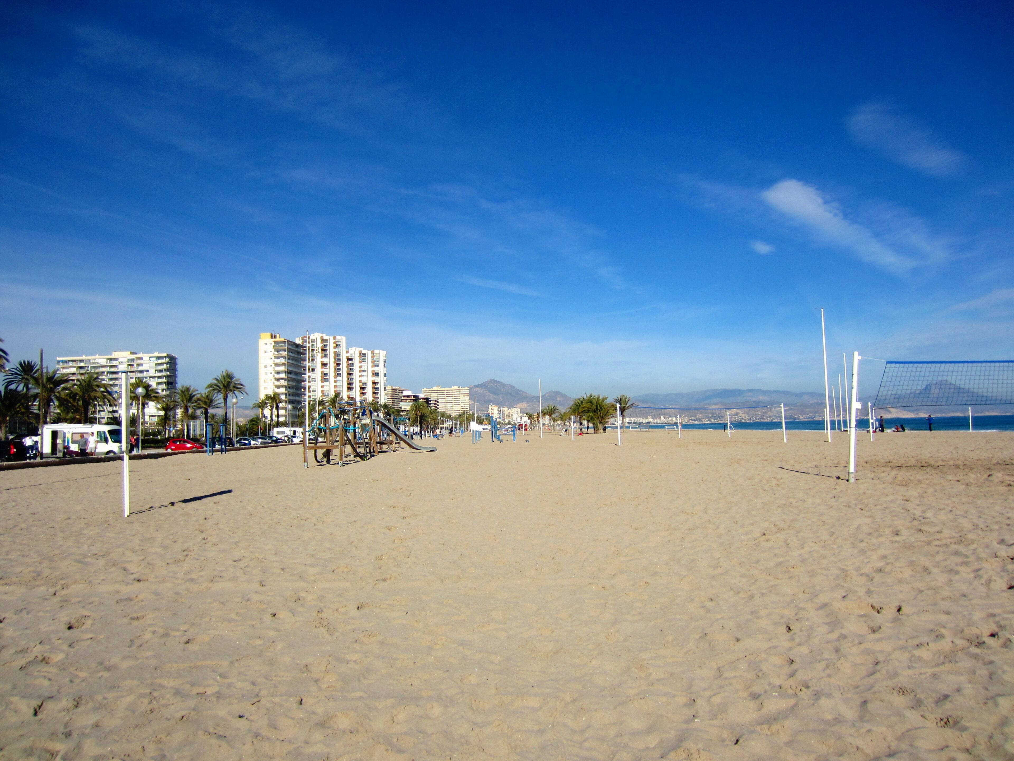 A sandy beach with volleyball nets, palm trees, and high-rise buildings in the background.