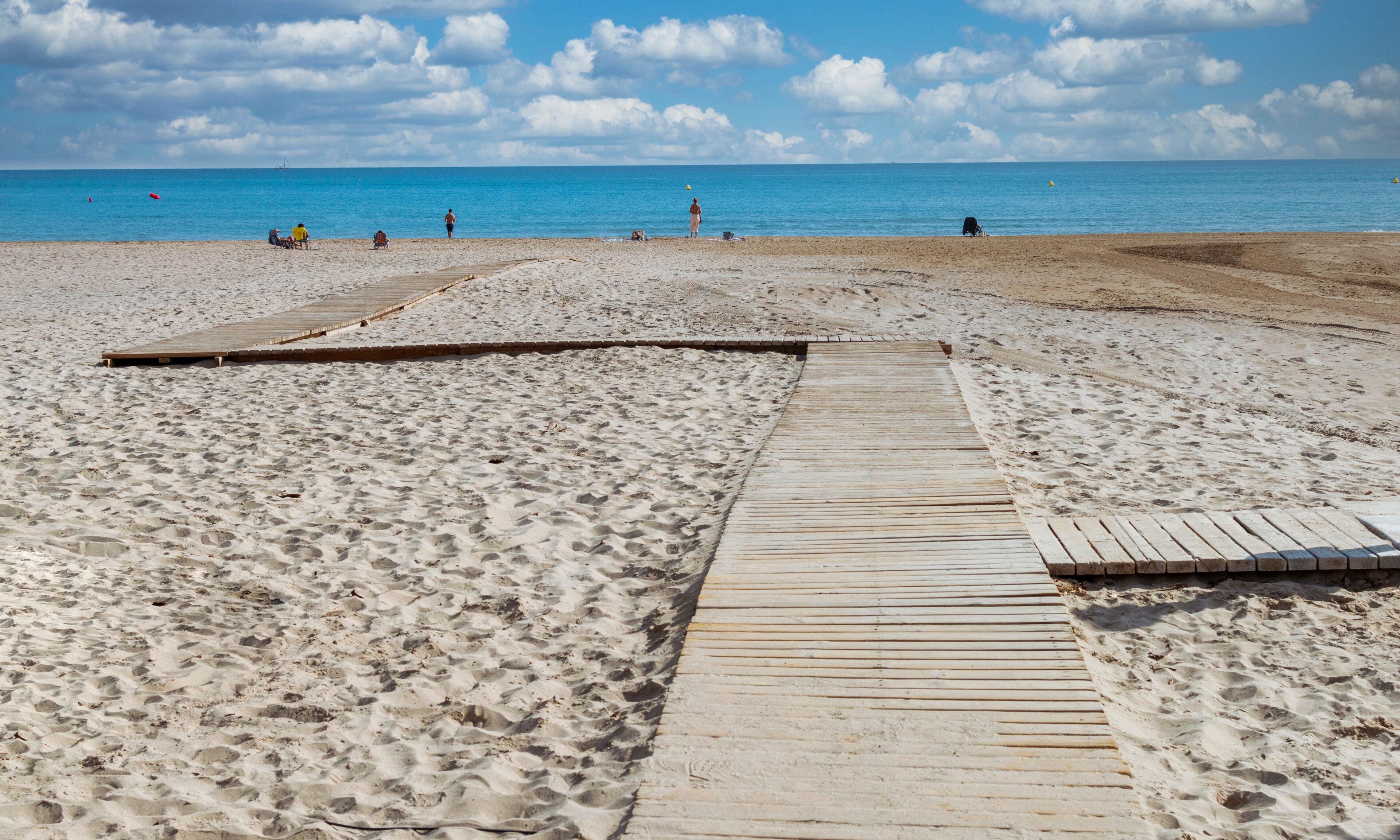 A sandy beach with a wooden boardwalk leading to the water.