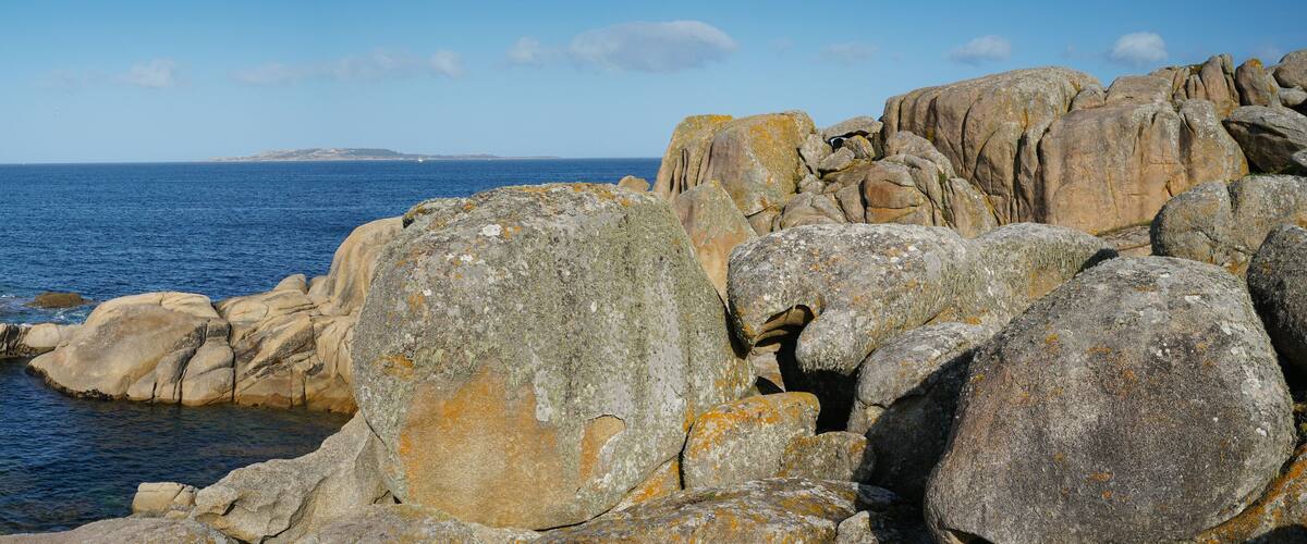 A rocky coastline with large boulders and a calm sea.