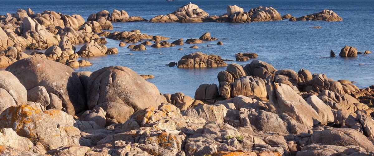 A rocky shoreline with large boulders and a clear blue sea.