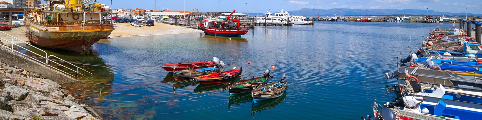 A harbor with boats docked along the shore, a sandy beach, and a clear blue sky.