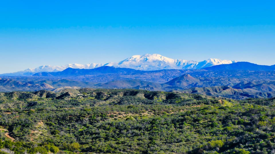 A mountain range with snow-capped peaks and a valley with dense vegetation.