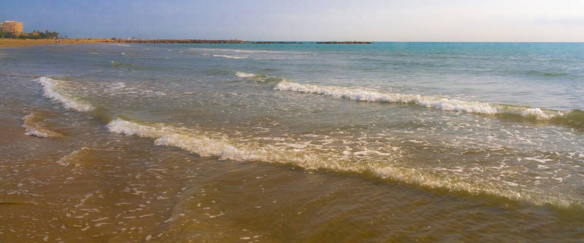 A beach with gentle waves, a clear sky, and a distant pier.