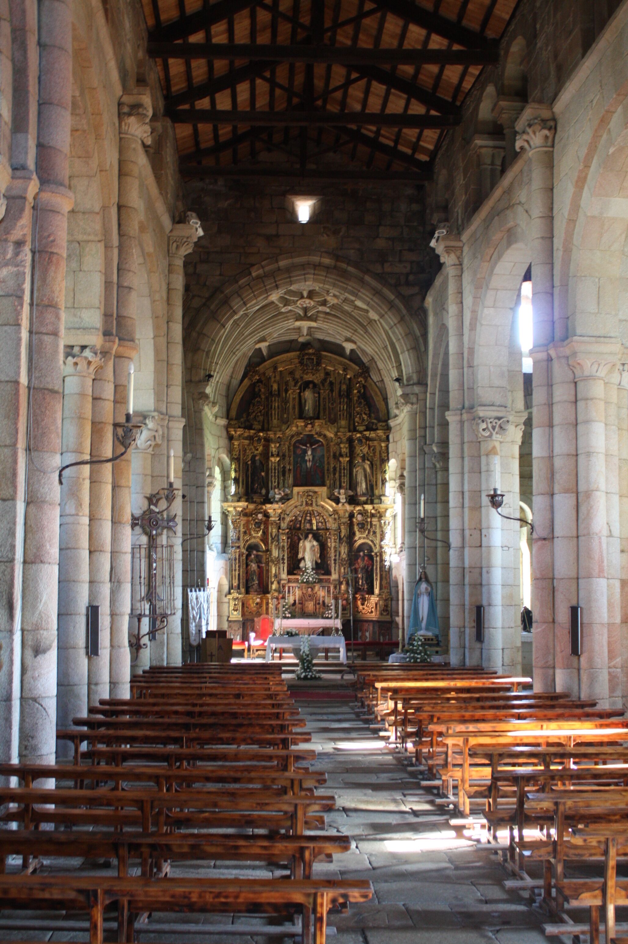 An interior of a church with rows of wooden pews, stone columns, and an ornate altar.