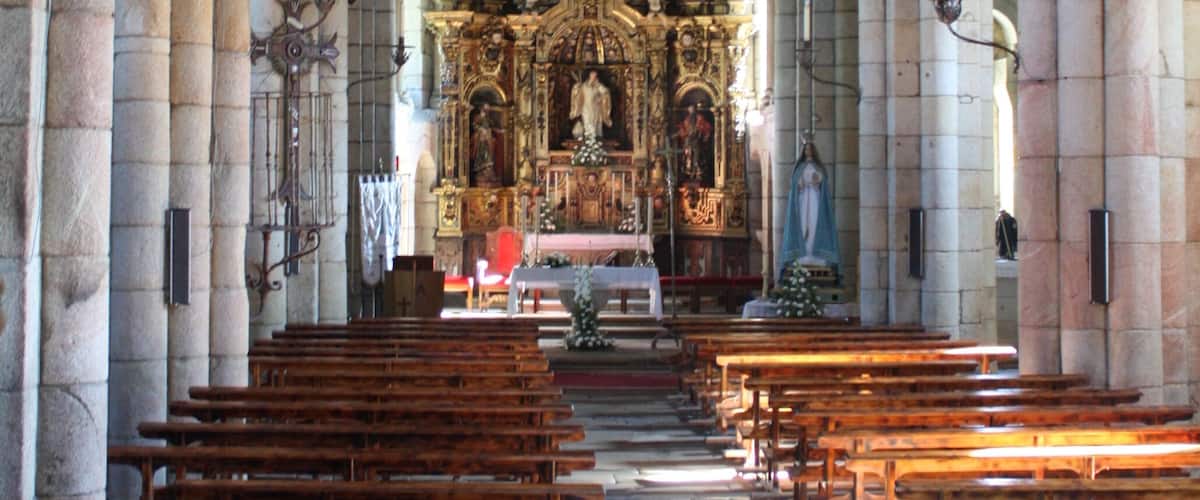 An interior of a church with rows of wooden pews, stone columns, and an ornate altar.