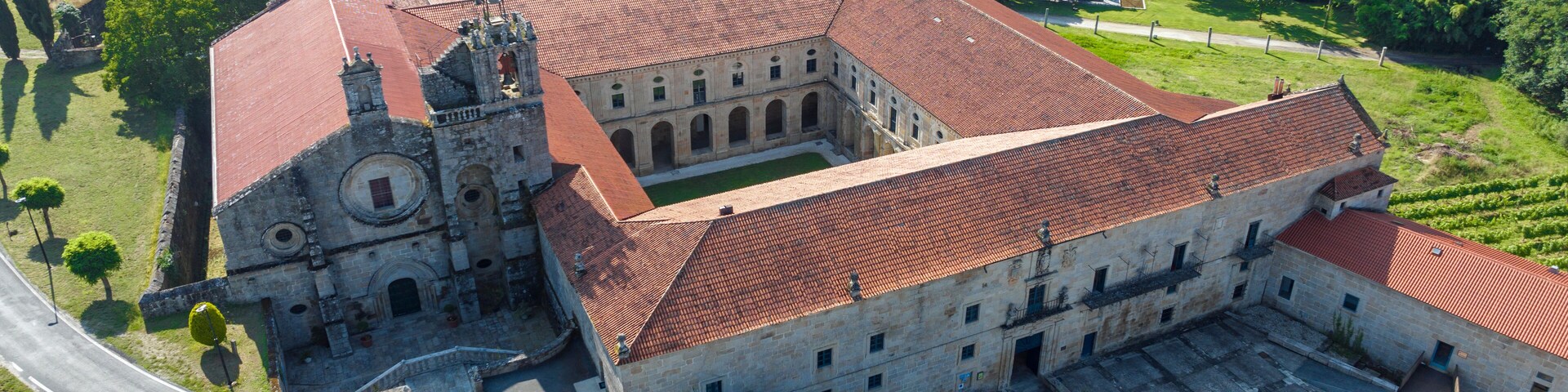 Vista aérea de un complejo de edificios históricos con tejados de tejas rojas, rodeado de exuberante vegetación y viñedos.